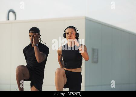 Two athletes doing warming-up exercises on a roof at sunset. Man and woman doing high-intensity exercises together Stock Photo