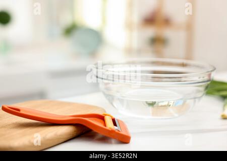 Orange peeler, board and bowl of water on white marble table indoors, closeup Stock Photo
