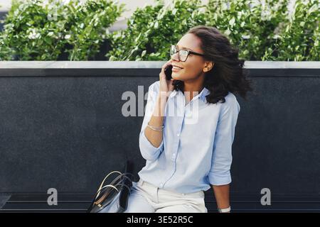 Female entrepreneur sitting outdoors using mobile phone Stock Photo