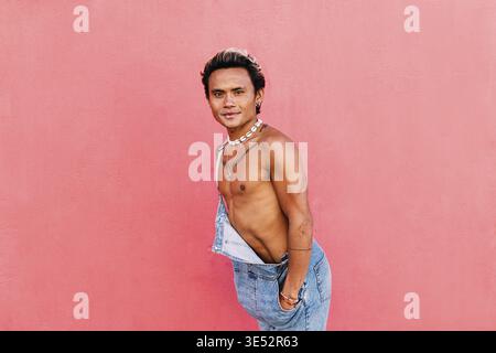 Young handsome guy posing outdoors against pink wall looking at camera Stock Photo