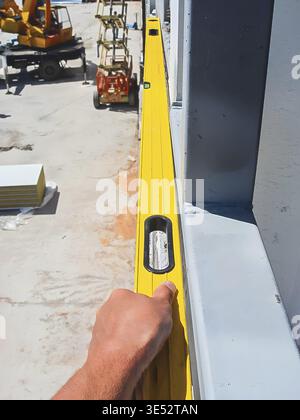 A construction worker uses a spirit level to ensure a structure is perfectly aligned, with construction equipment visible in the background Stock Photo