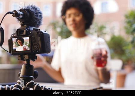 Woman with a juice in one hand talking to digital camera. Vlogger recording content Stock Photo