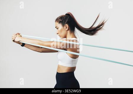 Side view of sportswoman exercising with resistance band against white wall Stock Photo