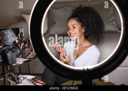 Smiling vlogger showing lipstick brush while recording a video Stock Photo