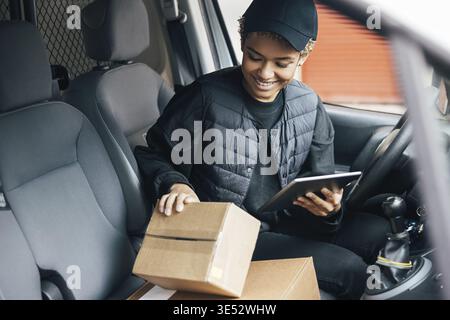 Young smiling woman in uniform checking the package for delivering in car Stock Photo