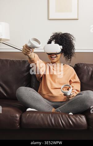 Young cheerful woman relaxing at home using virtual reality headset on couch Stock Photo
