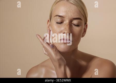 Beautiful female applying moisturizer on face in studio Stock Photo