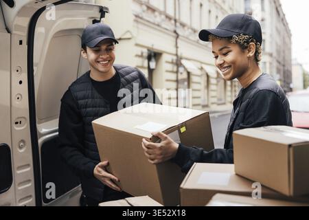 Two smiling couriers unloading cardboard boxes from van in the city Stock Photo