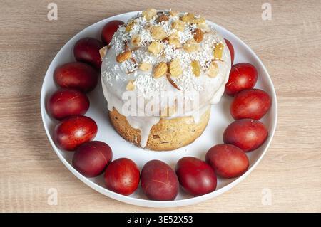 Close-up of traditional Easter cake decorated with icing, nuts, and coconut flakes, surrounded by red-dyed eggs, ready for celebration Stock Photo