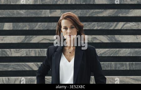 Portrait of a middle-aged female in black formal wear looking at camera. Confident businesswoman posing while standing outdoors Stock Photo