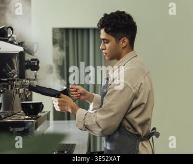Side view of a male barista in an apron using a coffee machine. Barista using preparing cappuccino Stock Photo