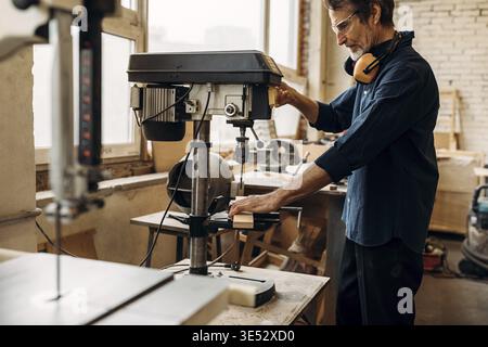 Carpenter drilling wood on machine. Male carpenter working in his workshop Stock Photo