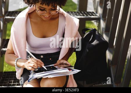Young graphic designer sitting on stairs outdoors, working on digital tablet Stock Photo