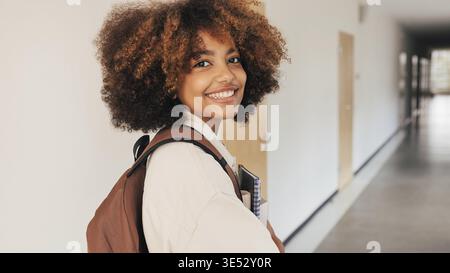 Smiling girl looking back while walking in high school corridor Stock Photo