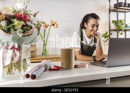 Smiling flower shop owner using laptop computer. Female florist working on laptop at counter Stock Photo