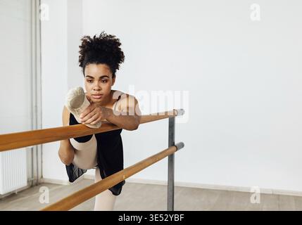 Ballerina stretching her leg on barre while practicing ballet dance in studio Stock Photo