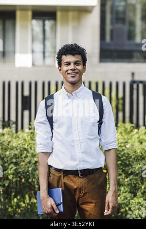 Handsome young man going standing outdoors with backpack and notebook Stock Photo