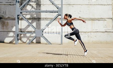 Full length shot of young female athlete sprinting in city. Slim woman running in the morning Stock Photo
