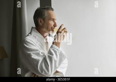 Side view of an elderly man drinking wine while looking at window in living room Stock Photo