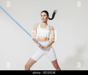 Healthy slim woman in white sports clothes practicing with resistance band in studio Stock Photo