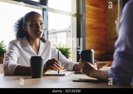 Two managers discussing in cafe. Woman talking with unrecognizable person Stock Photo