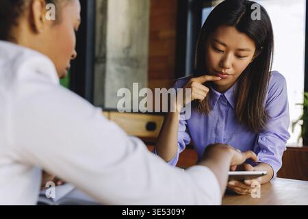 Two colleagues discussing new project, using digital tablet while sitting at table Stock Photo