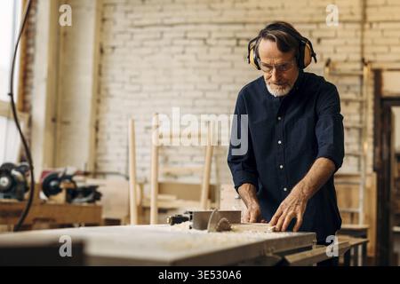 Senior carpenter in noise cancelling headphones working on saw machine Stock Photo