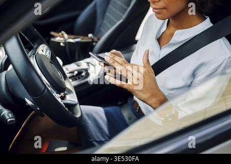 Unrecognizable woman using smartphone while sitting in car Stock Photo