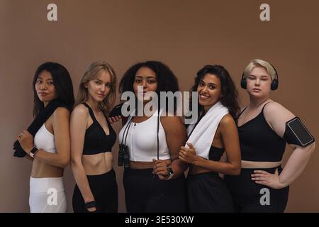 Group portrait of a five women in sportswear standing together on brown background Stock Photo