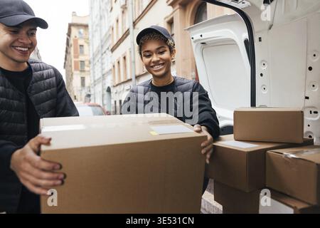 Two smiling coworkers unloading cardboard boxes from van for delivery Stock Photo