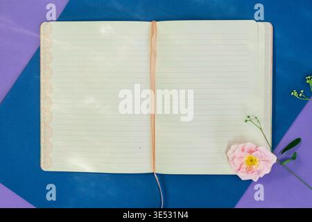 Open Lined Notebook with Ribbon Bookmark and Pink Flower on Blue and Purple Background Stock Photo
