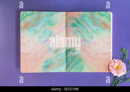 Open Notebook with Abstract Pastel Pages and Pink Flower on Purple Background – Creative Mockup Template Stock Photo