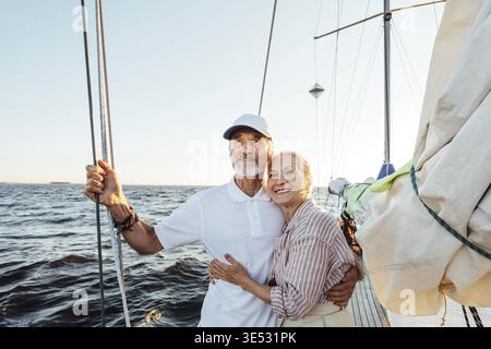 Loving senior couple enjoying vacation and looking to the distance. Mature couple standing together and embracing on a private sailboat Stock Photo