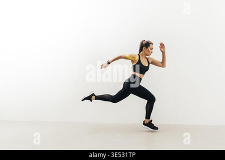 Side view of female athlete sprinting near a white wall Stock Photo