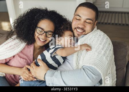 Happy family sitting on a couch at home. Mother, father, and their son embracing with closed eyes Stock Photo