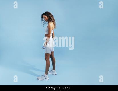 Fit woman posing on blue background. Side view of young sports woman relaxing Stock Photo