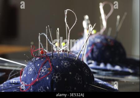 Different sewing needels and threads on a blue pincushion Stock Photo