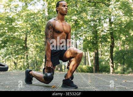 Man exercising with kettlebell outdoors. Athlete doing squats using kettlebells Stock Photo