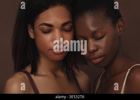 Close up of two beautiful women. Females with closed eyes head to head against a brown backdrop Stock Photo