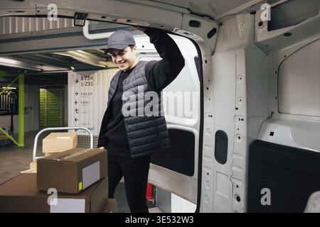 Confident courier leaning on van looking on cardboard boxes Stock Photo