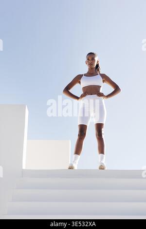 Full length of young slim sportswoman relaxing. Woman with hands on hips standing on the top of stairs Stock Photo