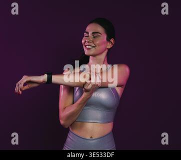 Young smiling female with closed eyes stretching and flexing her hands over magenta background in studio Stock Photo