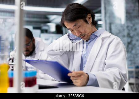 Senior researcher records observations from laboratory experiment for research documentation and scientific publication. Asian man in lab doing data logging, taking notes, preparing clinical reports Stock Photo