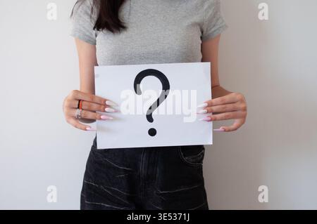 person holding question mark sign against plain wall, concept of uncertainty, inquiry Stock Photo