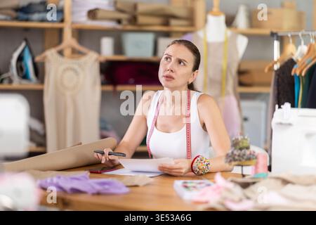 Young tailoress engaged in paperwork in sewing workshop Stock Photo