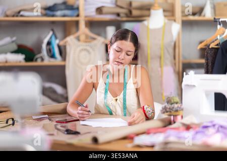 Young tailoress engaged in paperwork in sewing workshop Stock Photo