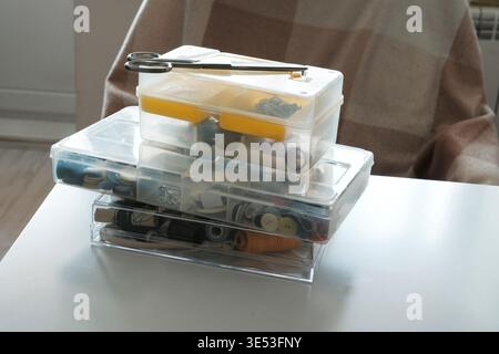 Stack of plastic organizers with sewing supplies and scissors on white table. Stock Photo