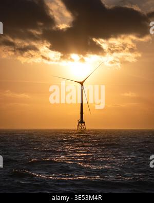 Offshore wind turbines silhouetted against a blazing amber sunset over the North Sea, crepuscular rays breaking through cloud behind the turbine. Stock Photo