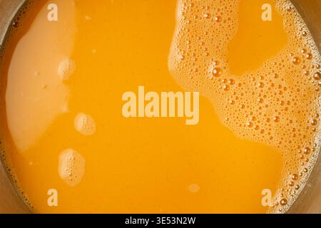 beaten liquid eggs in a container, vibrant orange egg yolk mixture, top view full frame texture with bubbles and foam, culinary preparation backdrop Stock Photo