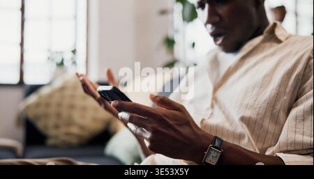 Hands, phone and texting on sofa in home with shock, gossip or fake news with post in living room. African man, smartphone and surprise with mobile Stock Photo